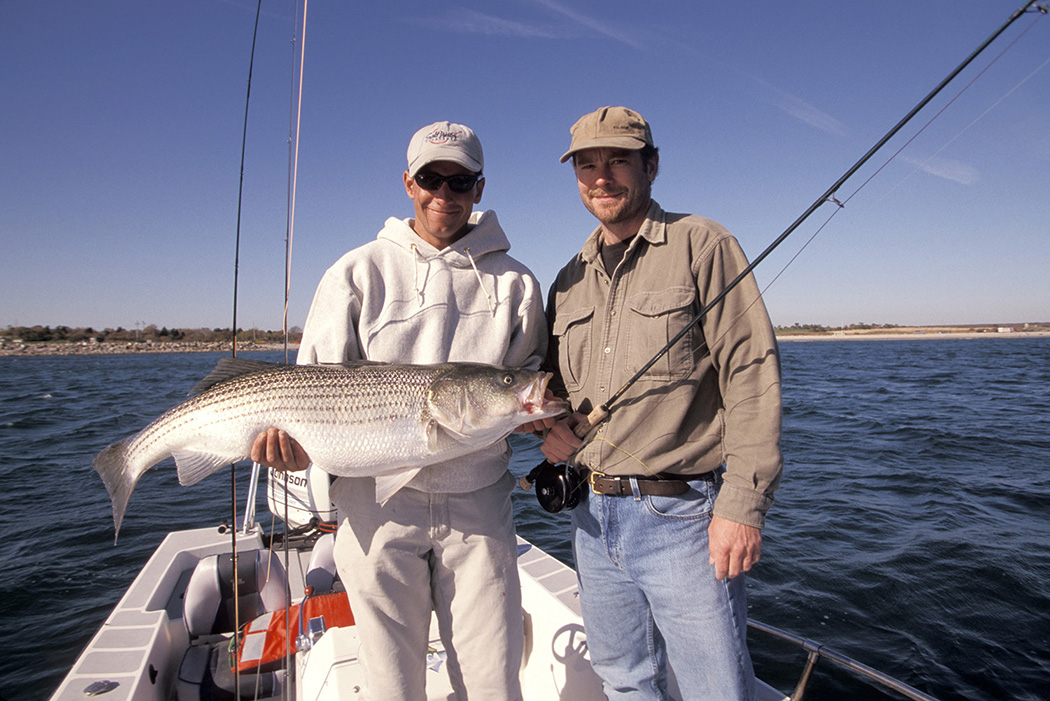 picture of two anglers on a boat holding a striped bass